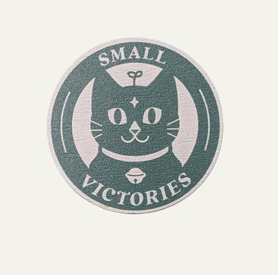 Circular wooden pin with a cat illustration and 'Small Victories' text on a white background